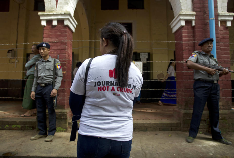 A journalist stands as polices stand guard outside the court during the trial of two Reuters journalists Monday, Sept. 3, 2018, in Yangon, Myanmar. A Myanmar court sentenced two Reuters journalists, Wa Lone and Kyaw Soe Oo, to seven years in prison Monday for illegal possession of official documents, a ruling that comes as international criticism mounts over the military's alleged human rights abuses against Rohingya Muslims. (AP Photo/Thein Zaw)