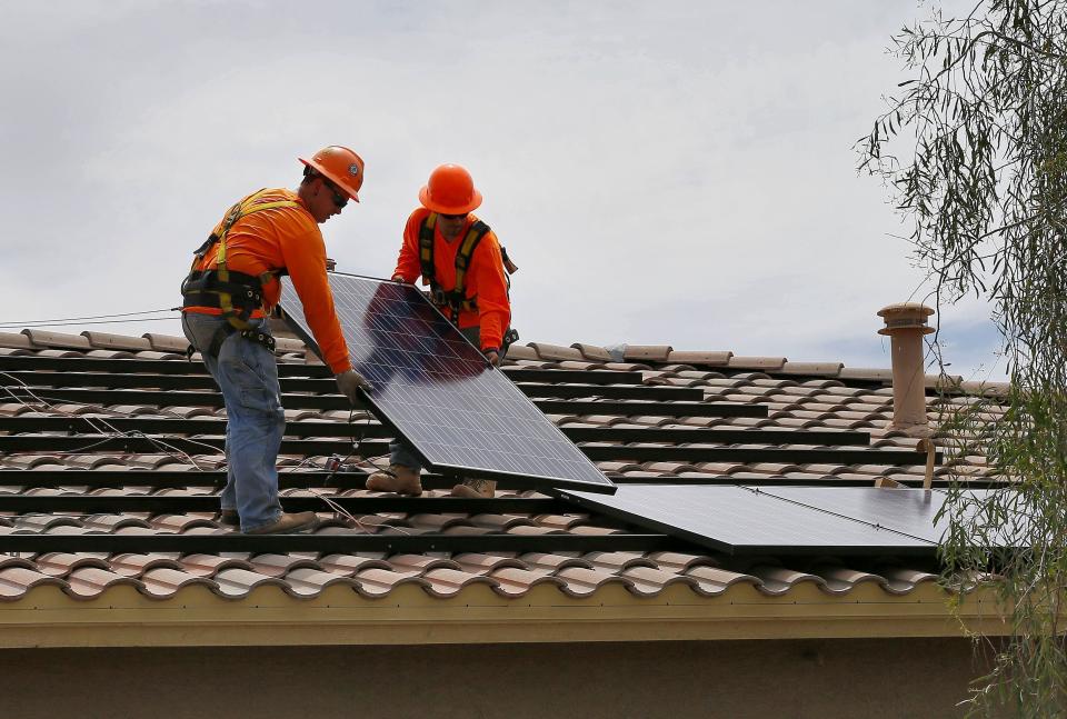 Electricians install solar panels on the roof of a home in Goodyear.