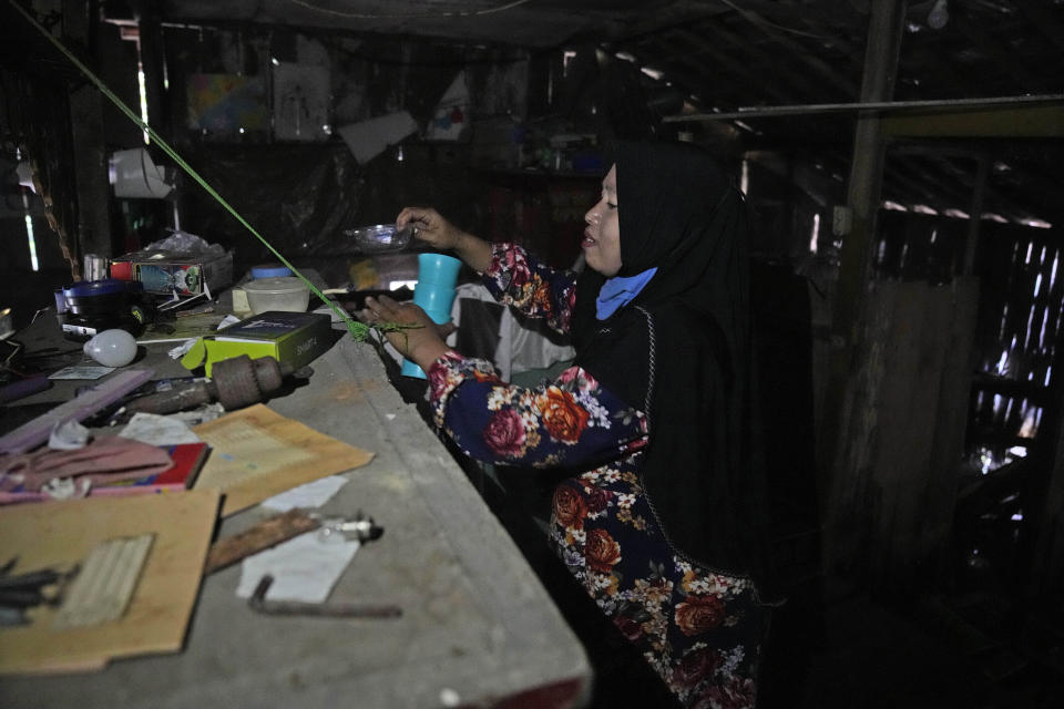 Asiyah, shifts through items left at her family's home they abandoned due to flooding in Mondoliko, Central Java, Indonesia, Monday, Sept. 5, 2022. She and her family eventually moved to drier land, becoming climate migrants as many of their neighbors had before them. (AP Photo/Dita Alangkara)