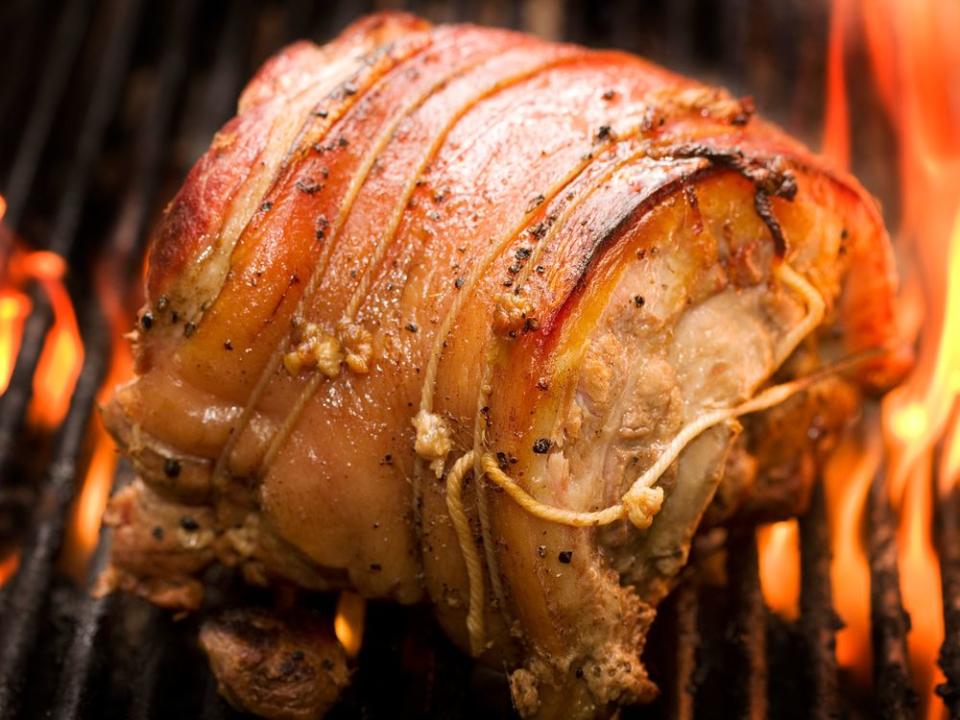 A pork roast on a grill with flames. | foodandwinephotography/Getty Images