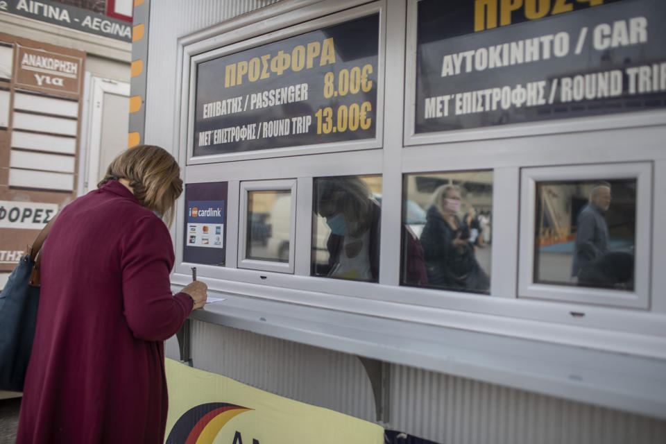 A passenger wearing a mask to curb the spread of the coronavirus fills in a travel document before she boards a ferry at the Piraeus port near Athens on Monday, May 25, 2020. Greece restarted Monday regular ferry services to the islands as the country accelerated efforts to salvage its tourism season.(AP Photo/Petros Giannakouris)