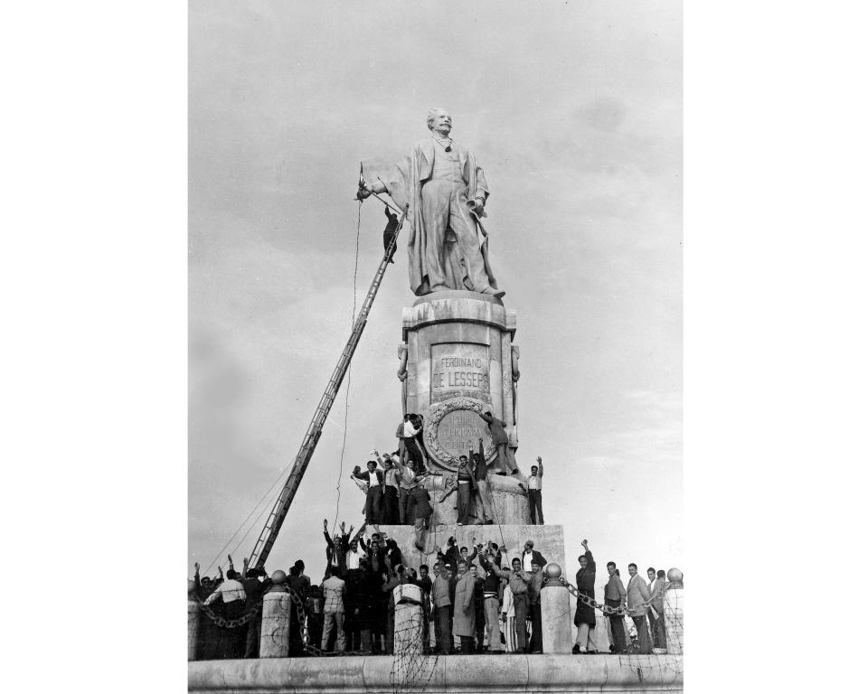 FILE - In this Dec. 24, 1956 file photo, Egyptian civilians climb on the statue of Ferdinand de Lesseps, the French diplomat who was behind the construction of Egypt's Suez Canal, in Port Said, prior to blowing it up. A proposal to bring back the statue has stirred controversy in Egypt with many saying it would be a salute to colonial times and a “humiliation" to the memory of tens of thousands of Egyptian laborers who died while digging the waterway. The debate started when a newspaper reported in June 2020 that local authorities in the Mediterranean province of Port Said were thinking of returning the statue to where it once stood at the northern entrance of the canal. (AP Photo, File)