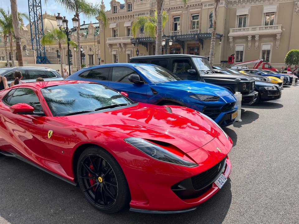 A row of fancy cars lined up in front of the Casino Monte Carlo including a red Ferrari in front.