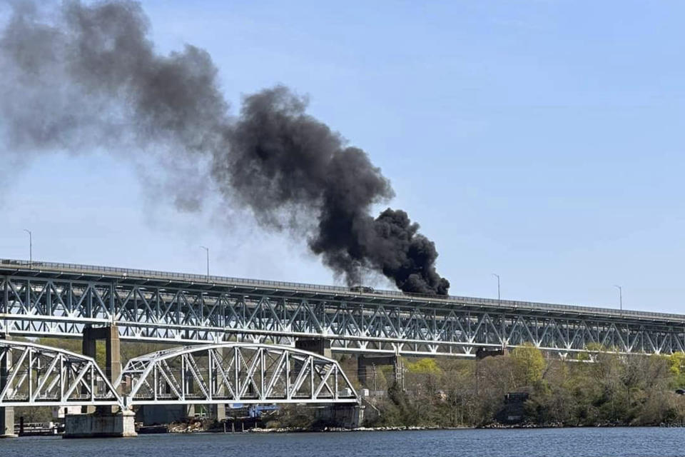 In this photo provided by the Connecticut State Police, plumes of smoke rise from a fire resulting from crash involving a fuel truck and a car on the Gold Star Memorial Bridge in Groton, CT., Friday, April 21, 2023. Flames spread to buildings below, causing officials to close Interstate 95 in both directions during the blaze. (Connecticut State Police via AP)