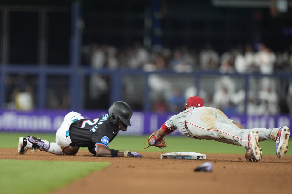 Philadelphia Phillies shortstop Edmundo Sosa, right, dives to attempt to tag out Miami Marlins' Jazz Chisholm Jr., after Chisholm hit a double during the seventh inning of a baseball game, Friday, May 10, 2024, in Miami. (AP Photo/Wilfredo Lee)