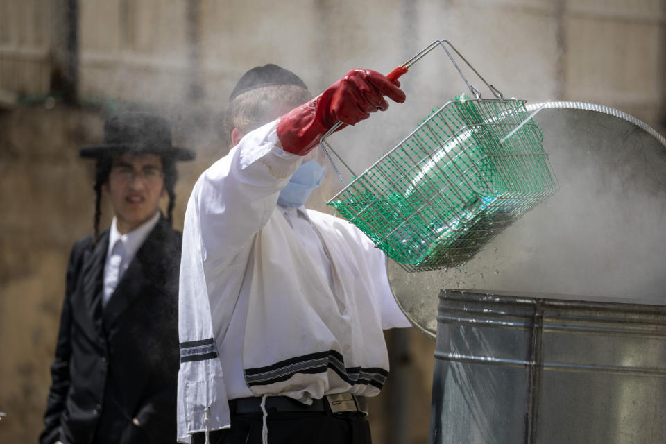 An ultra-Orthodox Jewish man wears a face mask and gloves following the government's measures to help stop the spread of the coronavirus, as he dips a basket with kitchen items into boiling water to cleanse them in preparation for the upcoming Jewish holiday of Passover in the Orthodox neighborhood of Mea Shearim in Jerusalem, Tuesday, April 7, 2020. Israeli Prime Minister Benjamin Netanyahu announced Monday a complete lockdown over the upcoming Passover feast to control the country's coronavirus outbreak, but offered citizens some hope by saying he expects to lift widespread restrictions after the week-long holiday. Passover starts on Wednesday on sundown. (AP Photo/Ariel Schalit)