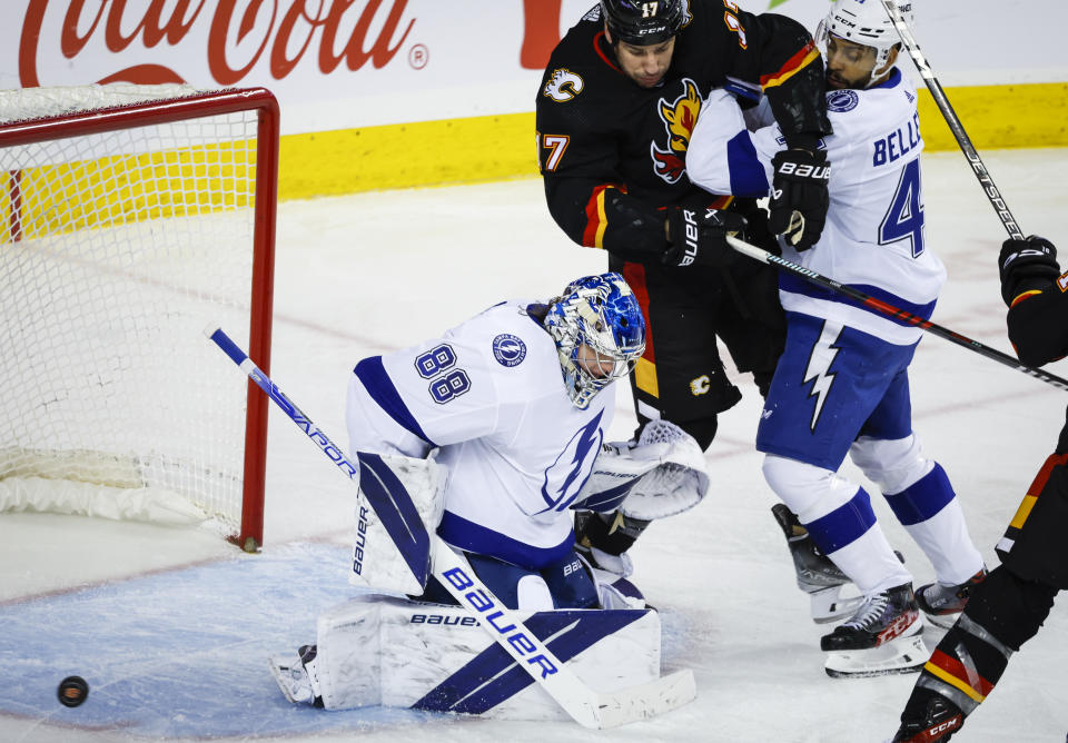 Tampa Bay Lightning forward Pierre-Edouard Bellemare, right, checks Calgary Flames forward Milan Lucic, center, as goalie Andrei Vasilevskiy looks for a loose puck during the third period of an NHL hockey game in Calgary, Alberta, Saturday, Jan. 21, 2023. (Jeff McIntosh/The Canadian Press via AP)