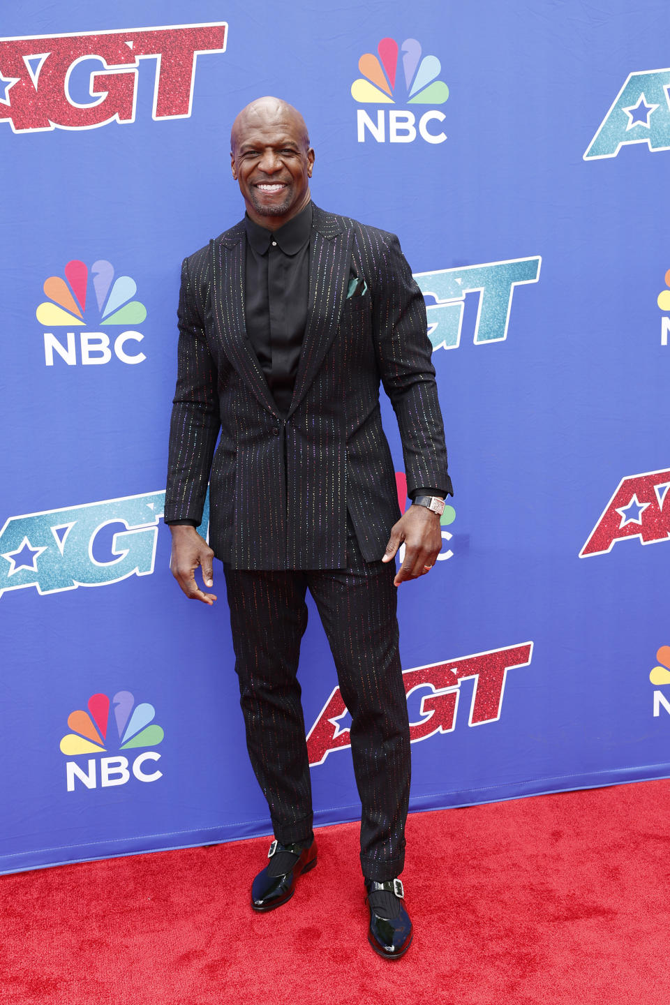 Terry Crews on the red carpet at an America's Got Talent event, wearing a pinstripe suit and a black shirt