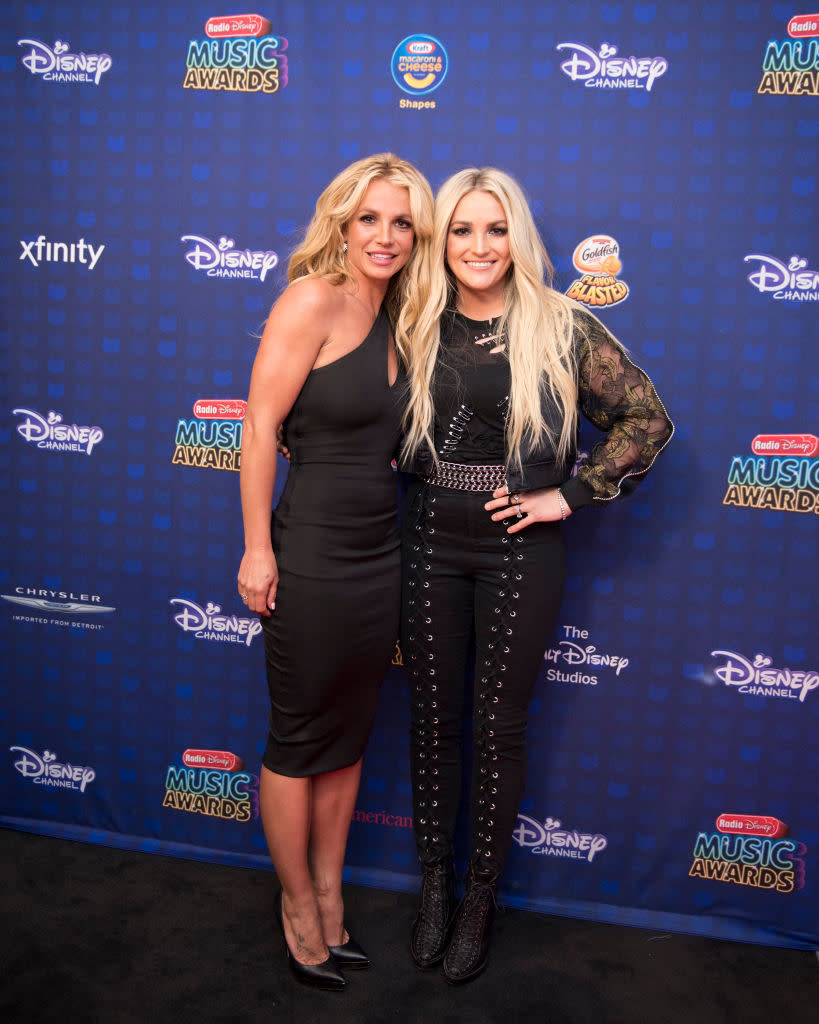 Britney and Jamie Lynn on an event backdrop, Britney in a sleeveless dress and Jamie in an embellished outfit