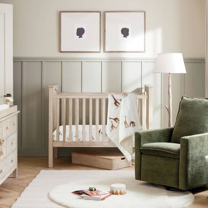 White crib with dark green arm chair and half wall paneling