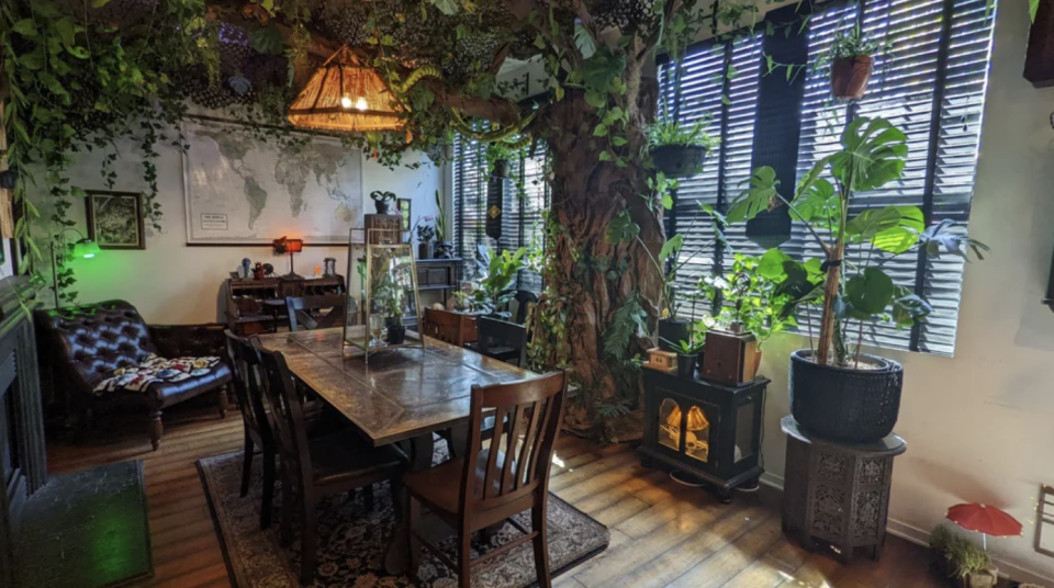 This dining room is jungle-themed and is surrounded by plants and has a fake tree arching over the table
