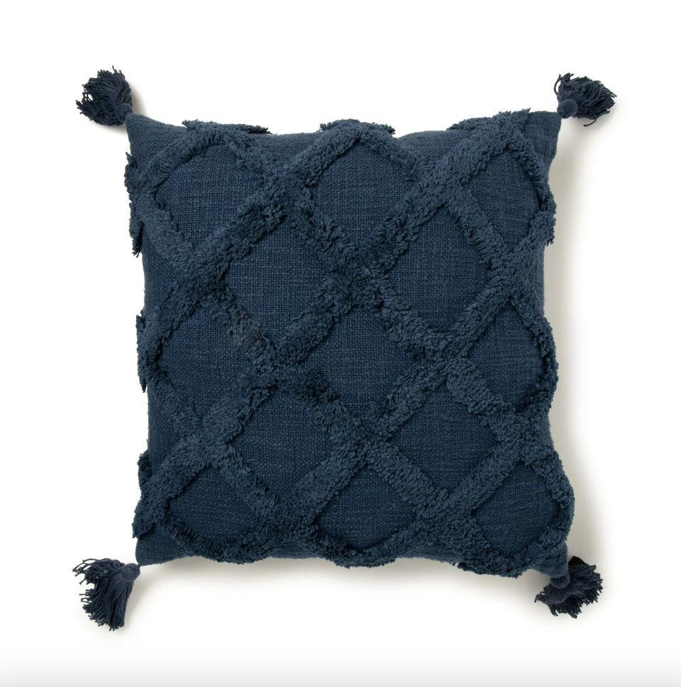 The coral pillow with a tufted trellis pattern resting on a chair