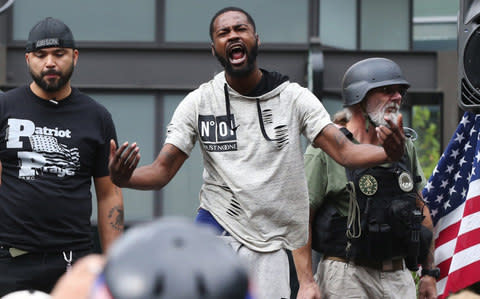 Conservative Joey Gibson, left, looks on after Black Lives Matter protester Arthur Ford, center, took the stage during a pro-Trump rally in Seattle - Credit: AP