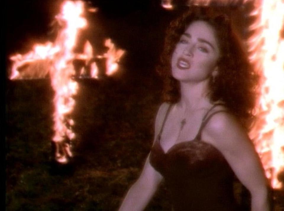 Madonna dancing in a bustier in front of a giant flaming cross