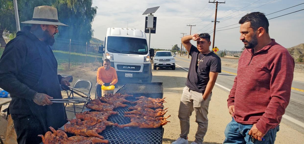 Customers watching as man grills chickens at a roadside stand