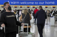 Passengers queue to check in, at Heathrow Airport in London, Monday, Nov. 29, 2021. The new potentially more contagious omicron variant of the coronavirus popped up in more European countries on Saturday, just days after being identified in South Africa, leaving governments around the world scrambling to stop the spread. In Britain, Prime Minister Boris Johnson said mask-wearing in shops and on public transport will be required, starting Tuesday. (AP Photo/Frank Augstein)