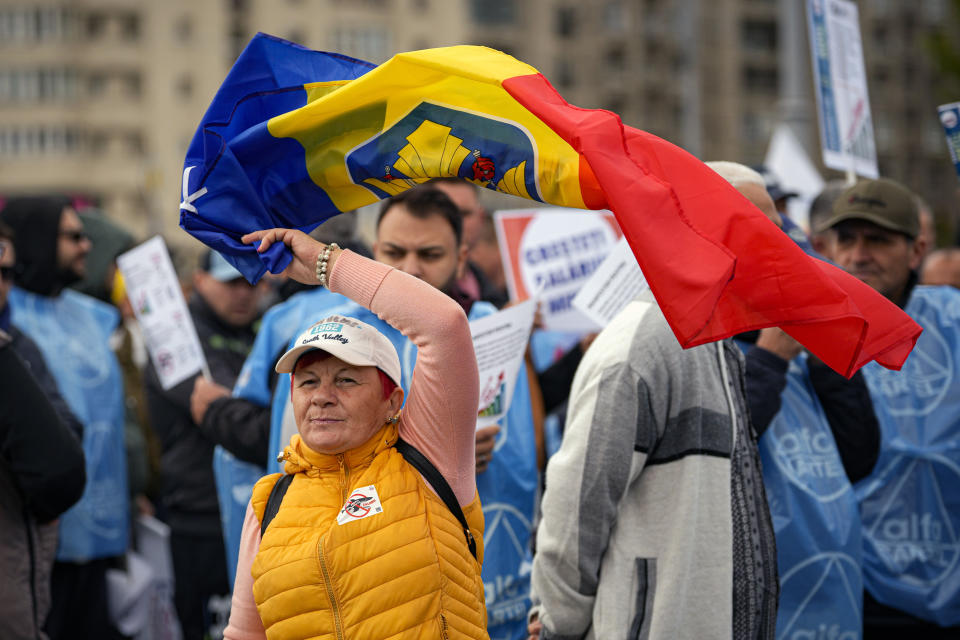 A woman waves a flag during a protest outside the government headquarters in Bucharest, Romania, Thursday, Oct. 20, 2022. People joined a protest dubbed "The Anti-Poverty March" demanding salary and pensions increases and government controlled prices for energy and other basic commodities. (AP Photo/Andreea Alexandru)