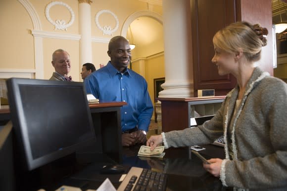 A bank teller smiles at a customer as she counts out money for him.