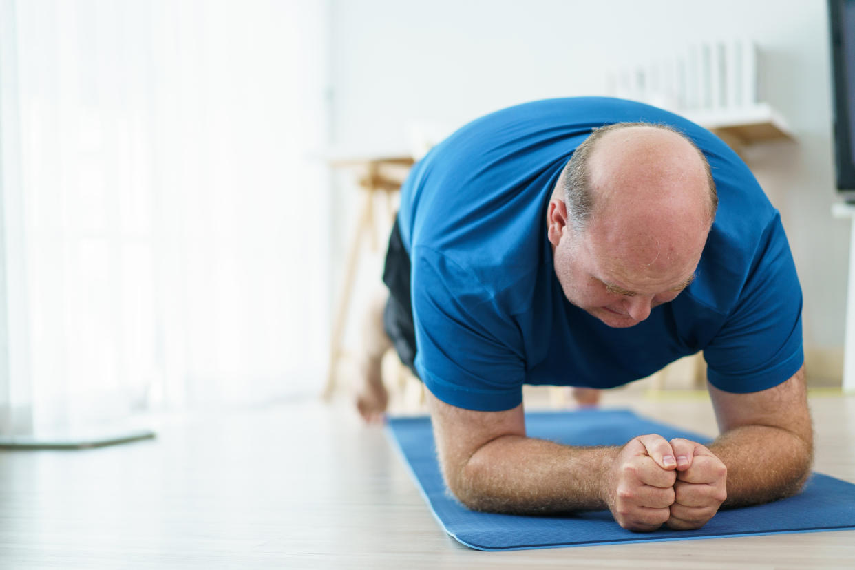 Very large body shape caucasian white man push his effort to exercise at home to improve his body shape and good health. Overweight man doing a body weight training at home in living room.