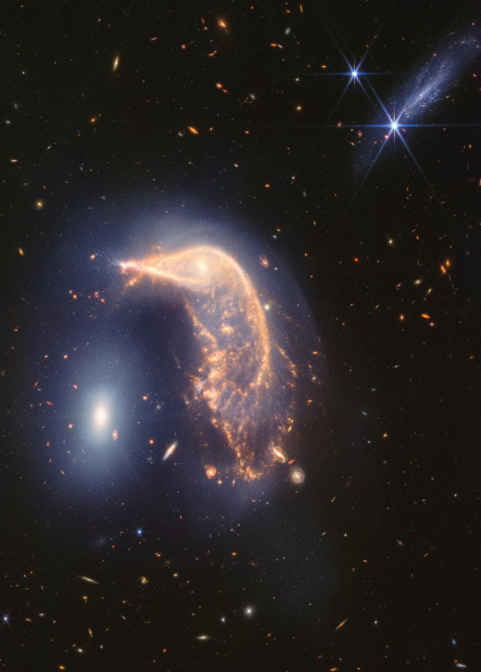 A photo taken by the James Webb Space Telescope shows the distorted spiral galaxy at center, the Penguin, and the compact elliptical galaxy at left, the Egg, locked in an active embrace.