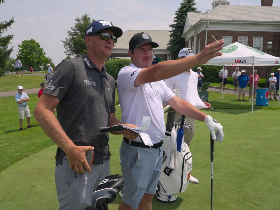 Two men wearing golf clothing stand on a green course.