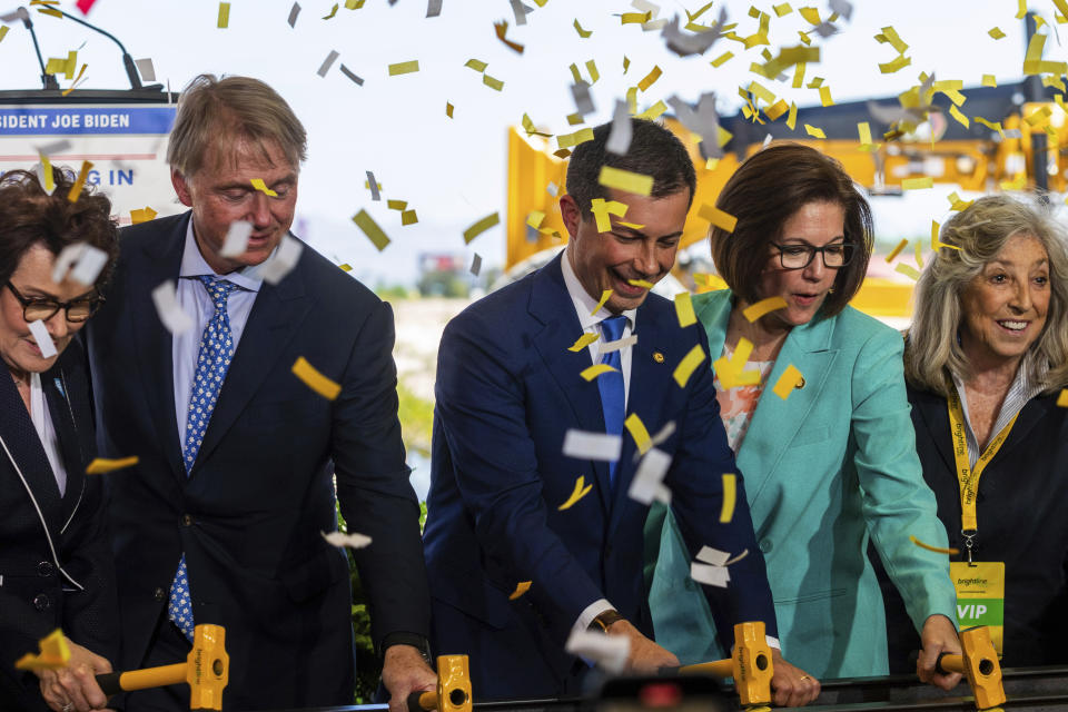 U.S. Secretary of Transportation Pete Buttigieg, center, Sen. Catherine Cortez Masto, right, drive rail spikes into a symbolic rail, on Monday, April 22, 2024, in Las Vegas. A $12 billion high-speed passenger rail line between Las Vegas and the Los Angeles area has started construction. (AP Photo/Ty ONeil)