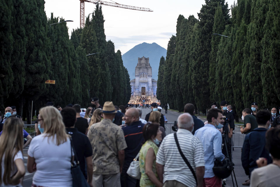 People gather to watch musicians performing in front of the Bergamo cemetery, Italy, Sunday, June 28, 2020. Italy bid farewell to its coronavirus dead on Sunday with a haunting Requiem concert performed at the entrance to the cemetery of Bergamo, the hardest-hit province in the onetime epicenter of the outbreak in Europe. President Sergio Mattarella was the guest of honor, and said his presence made clear that all of Italy was bowing down to honor Bergamo’s dead, “the thousands of men and women killed by a sickness that is still greatly unknown and continues to threaten the world.” (Claudio Furlan/LaPresse via AP)