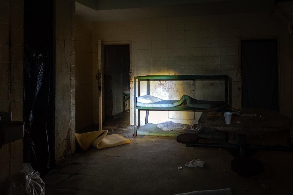 Bags of trash and dusty bed linens litter the remaining furniture and the floor of the old jail.