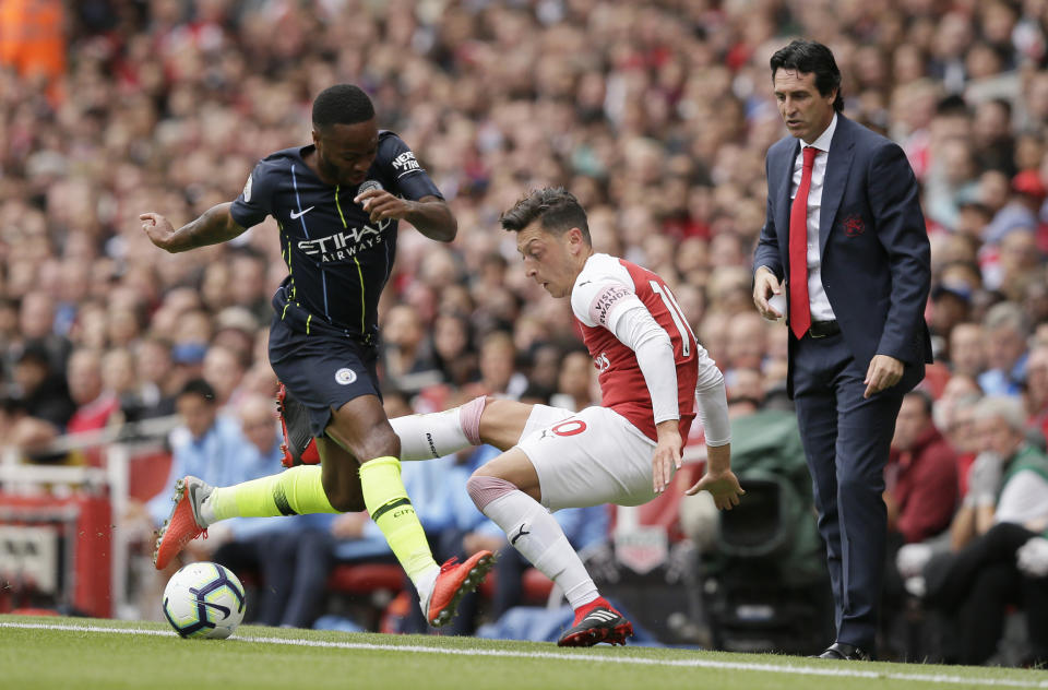 Arsenal manager Unai Emery, right, watches Manchester City's Raheem Sterling, left, fight for the ball with Arsenal's Mesut Ozil during the English Premier League soccer match between Arsenal and Manchester City at the Emirates stadium in London, England, Sunday, Aug. 12, 2018. (AP Photo/Tim Ireland)