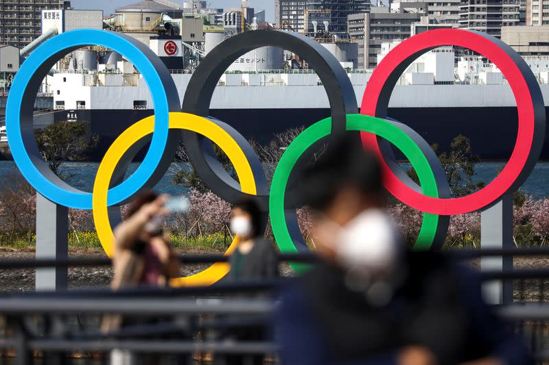 People wearing protective face masks are seen in front of the Giant Olympic rings at the waterfront area at Odaiba Marine Park in Tokyo