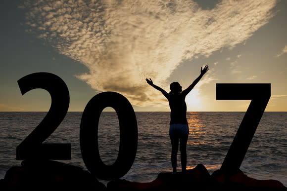 Picture of a woman watching the sun go down at the ocean with both arms raised to mimic the number 1 in 2017 next to her.