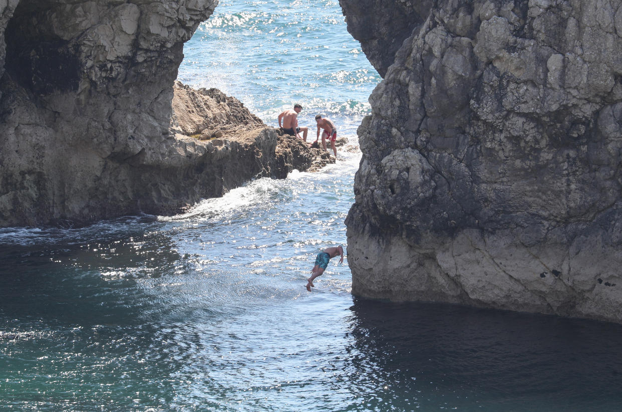 A person jumps into the sea from Durdle Door, near Lulworth, despite Dorset Council announcing that the beach was closed to the public after three people were seriously injured jumping off cliffs into the sea.