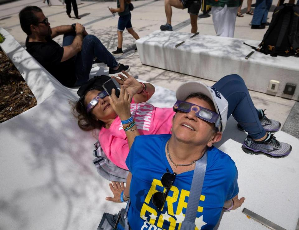 Malena Contreras, front, and Claudia Herman watch the partial solar eclipse from the plaza on Monday, April 8, 2024, at The Phillip and Patricia Frost Museum of Science in downtown Miami.