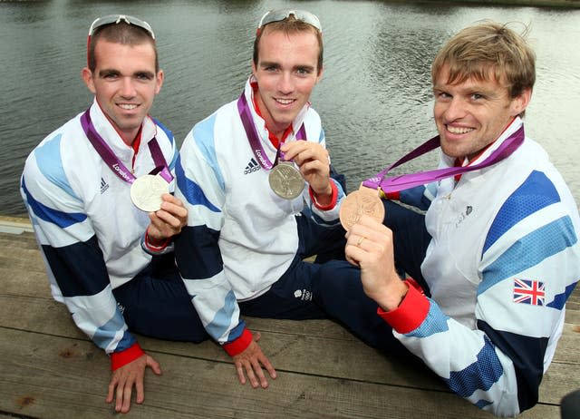 Three men sit on a jetty with their Olympic medals