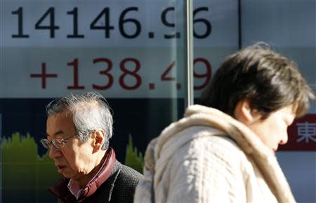 Pedestrians walk past an electronic board showing Japan's Nikkei average outside a brokerage in Tokyo February 5, 2014. REUTERS/Yuya Shino