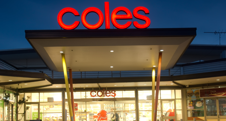 The storefront of a Coles supermarket is seen at dusk. 