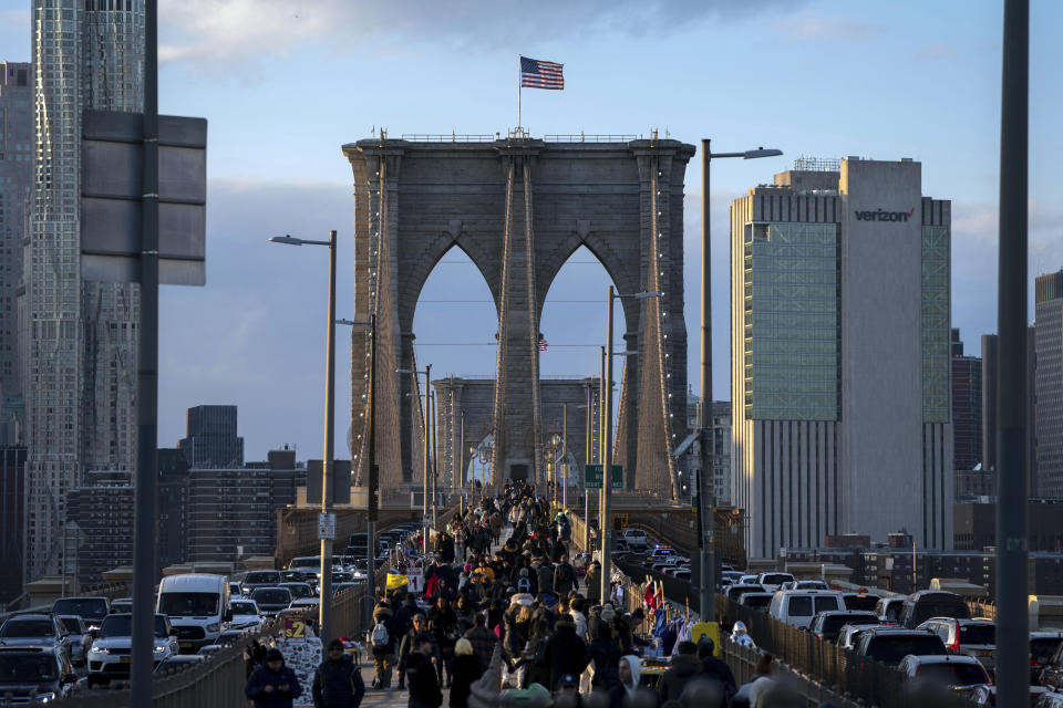 FILE - People walk on the Brooklyn Bridge at sunset, Nov. 18, 2022, in New York. metropolis is slowly sinking under the weight of its skyscrapers, homes, asphalt and humanity itself. (AP Photo/Julia Nikhinson, File)