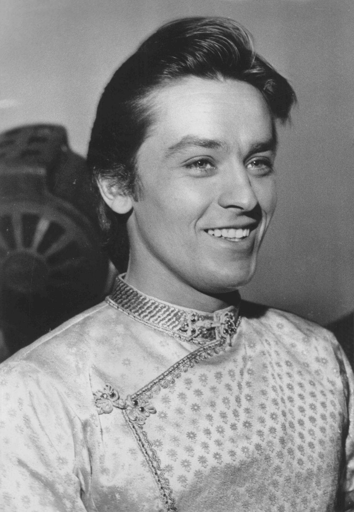 Black and white headshot of a young Alain Delon smiling