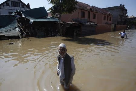 Kashmiri men pass a damaged house as they wade through a flooded street in Srinagar September 14, 2014. REUTERS/Danish Ismail