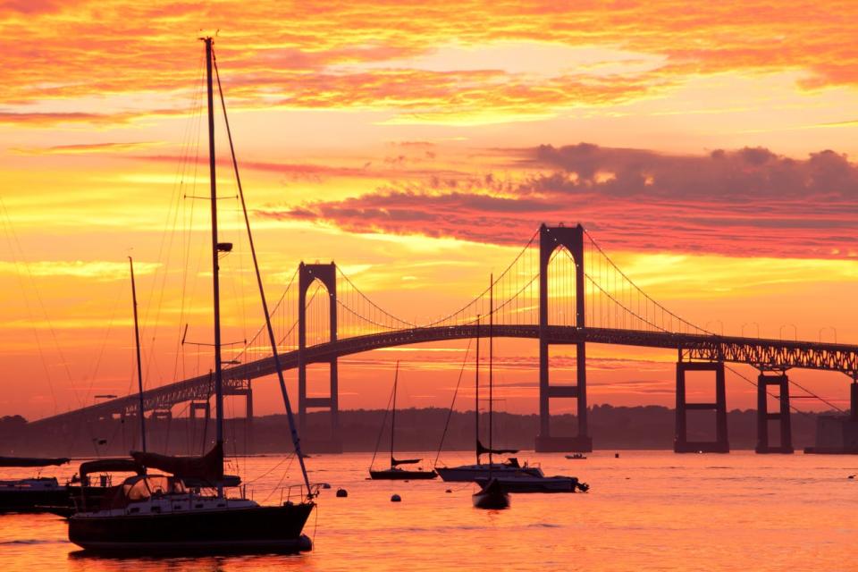 Sailboats in Newport Harbor are silhouetted against a fiery sunset