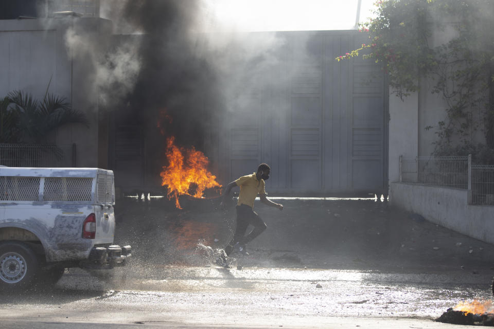 A factory worker runs past burning tires set on fire by workers during a protest demanding a salary increase, in Port-au-Prince, Haiti, Thursday, Feb. 10, 2022. The workers employed at factories that produce textiles and other goods say they make 500 gourdes ($5) a day for nine hours of work and are seeking a minimum of 1,500 gourdes ($15) a day. (AP Photo/Odelyn Joseph)