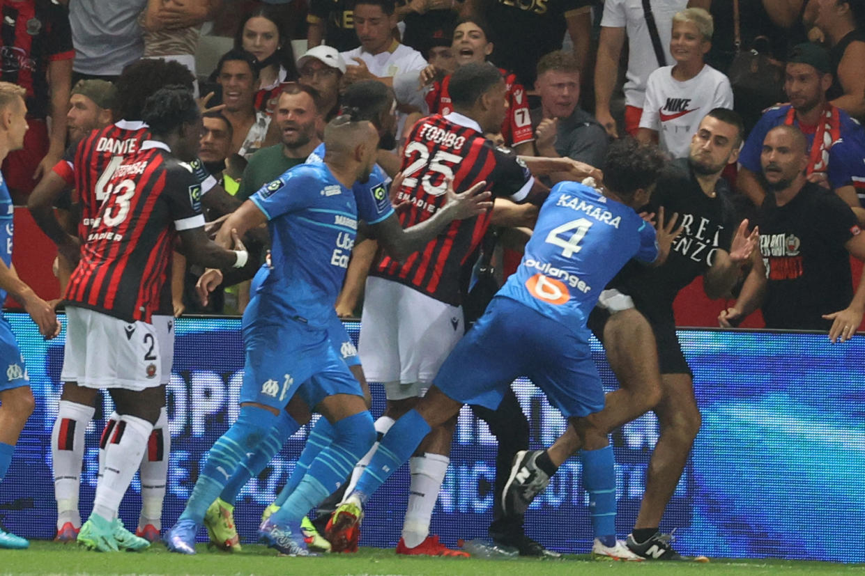 Marseille's French midfielder Dimitri Payet (2nd L) reacts as players from OGC Nice (red and black jersey) and Olympique de Marseille (blue jersey) stop a fan invading the pitch  during the French L1 football match between OGC Nice and Olympique de Marseille (OM) at the Allianz Riviera stadium in Nice, southern France on August 22, 2021. - The French Ligue 1 game between Nice and Marseille was halted on August 22, 2021, when fans of the home side invaded the pitch and angrily confronted opposing player Dimitri Payet. An AFP journalist at the game said trouble flared in the 75th minute when Marseille star Payet, who had been targeted by plastic bottles every time he took a corner, lobbed one back into the stands. (Photo by Valery HACHE / AFP) (Photo by VALERY HACHE/AFP via Getty Images)