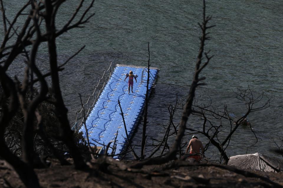 People swim at a beach in Rafina, east of Athens, Wednesday, Aug. 1, 2018, ten days after the the wildfire. The bodies of 76 people killed by Greece's deadliest wildfire in decades have been identified, authorities said Tuesday, as forensic experts kept working to identify more remains recovered from the charred resort area. (AP Photo/Thanassis Stavrakis)