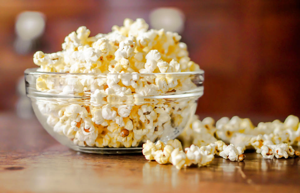 Closeup Popcorn in a glass cup on a wooden table and blurry background.