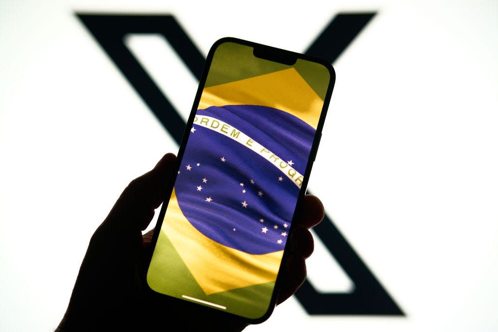 The X platform and logo are seen in the background, the Brazilian flag is displayed on a phone screen in the foreground.