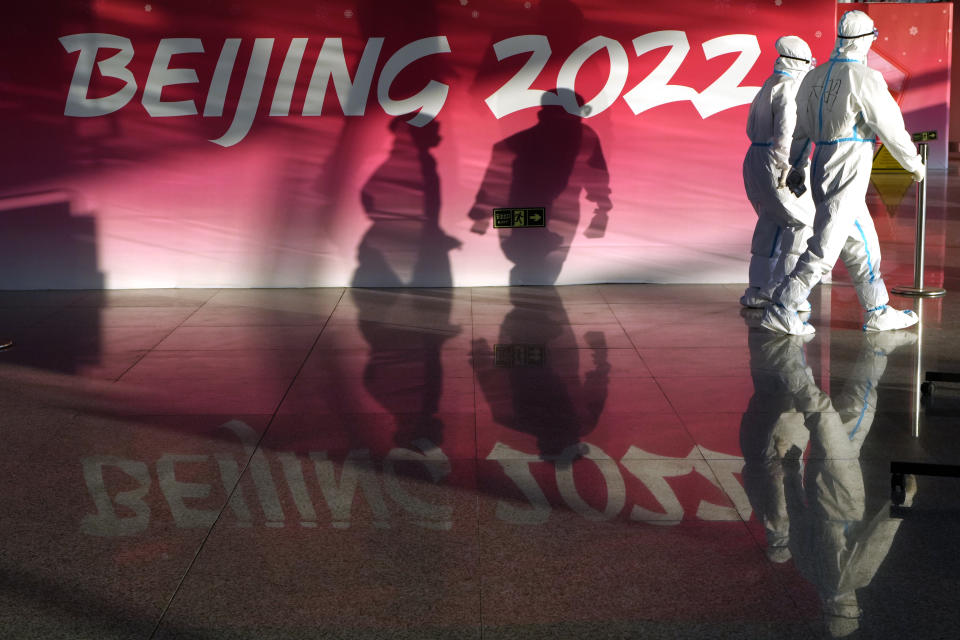 Empleados con ropa protectora se desplazan en el aeropuerto de Beijing al recibir a pasajeros previo a los Juegos de Invierno, el lunes 31 de enero de 2022. (AP Foto/Kirsty Wigglesworth)