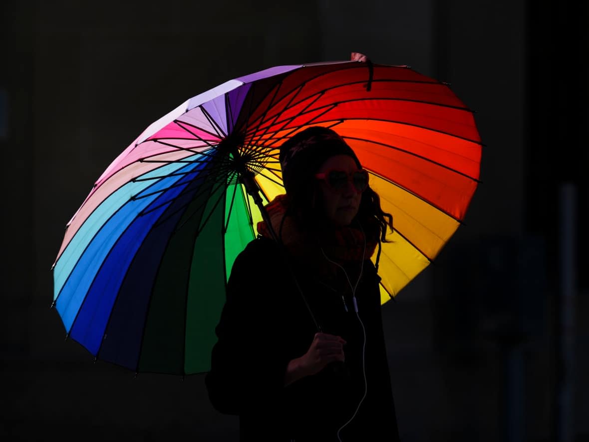 A person walks with a rainbow umbrella in Ottawa Sept. 30, 2022. (Sean Kilpatrick/The Canadian Press - image credit)