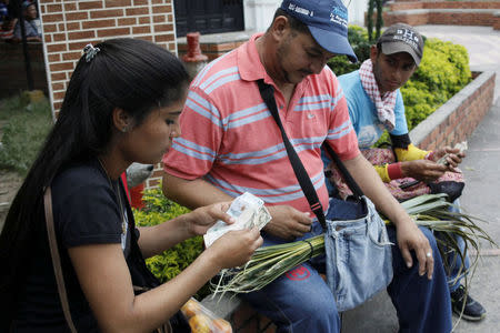 Genesis Materan (L) counts Colombian pesos as she sells vegetables and fruits bought in Venezuela to a customer in Cucuta, Colombia December 15, 2017. REUTERS/Carlos Eduardo Ramirez