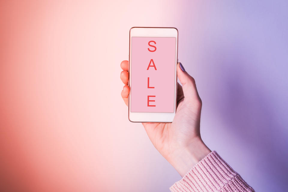 Close-Up Of Woman Hand Holding Mobile Phone Showing Sale Text Against Colored Background