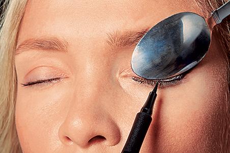 A woman using a spoon to create winged eyeliner